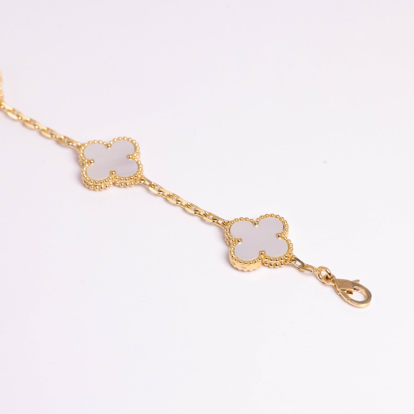 Gold bracelet with clover-shaped charms on a light pink background
