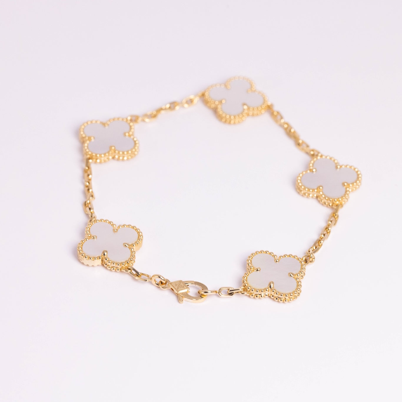 Gold bracelet with white clover-shaped charms on a light gray background