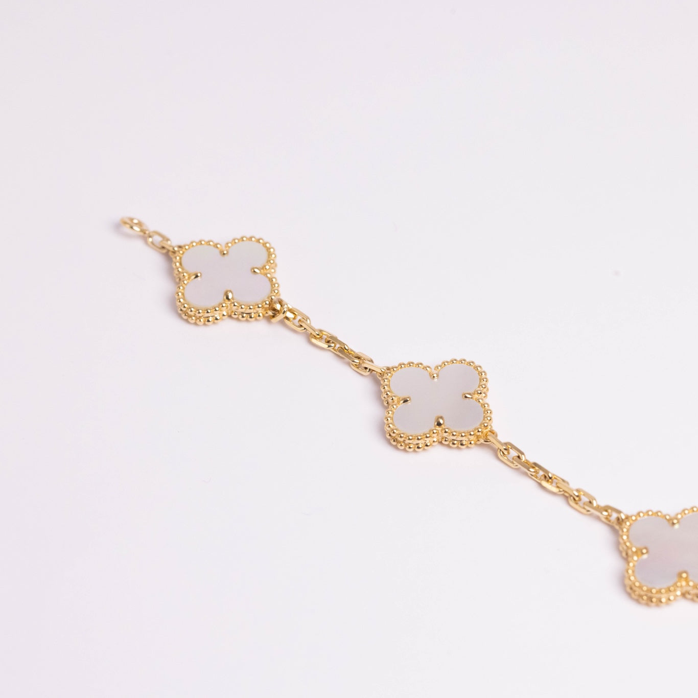 Gold bracelet with white clover-shaped charms on a light gray background